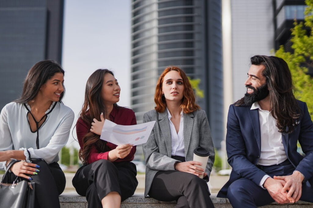 Diverse young business people sitting outside of office building