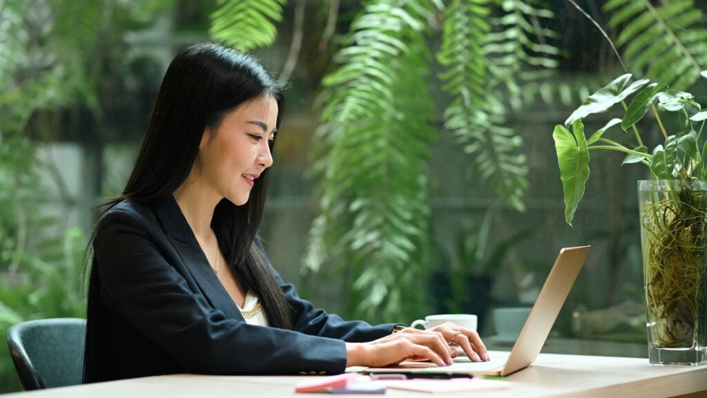 Smiling millennial businesswoman using laptop computer in green